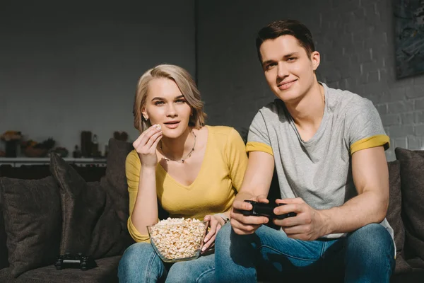 Girlfriend eating popcorn and watching boyfriend playing video game at home — Stock Photo