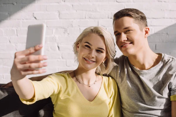 Улыбающаяся пара делает селфи со смартфоном дома — стоковое фото