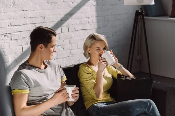 Happy couple drinking coffee on sofa at home — Stock Photo