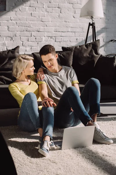 Пара, сидящая на полу в гостиной с ноутбуком — стоковое фото