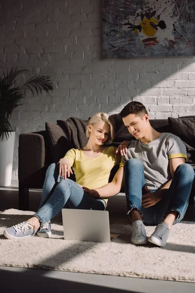 Пара, сидящая на полу и смотрящая кино на ноутбуке дома — стоковое фото