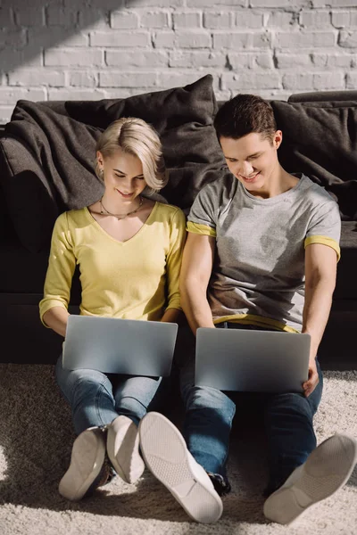 Couple assis sur le sol et utilisant deux ordinateurs portables à la maison — Photo de stock