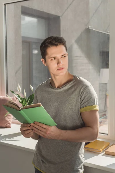 Красивый мужчина, держащий в руках книгу и отводящий взгляд от дома — стоковое фото