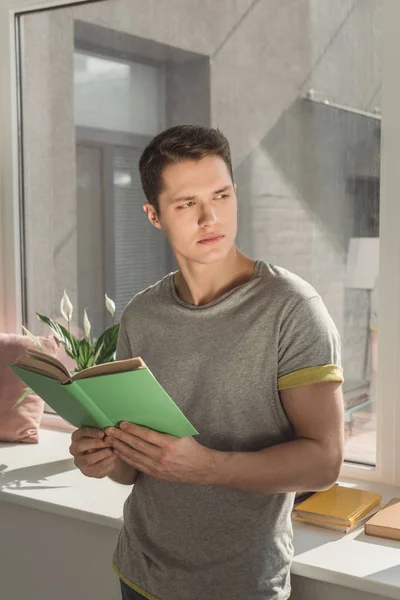 Beau homme tenant le livre et regardant loin à la maison — Photo de stock