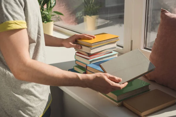 Abgeschnittenes Bild eines Mannes, der Bücher auf der Fensterbank hält — Stockfoto