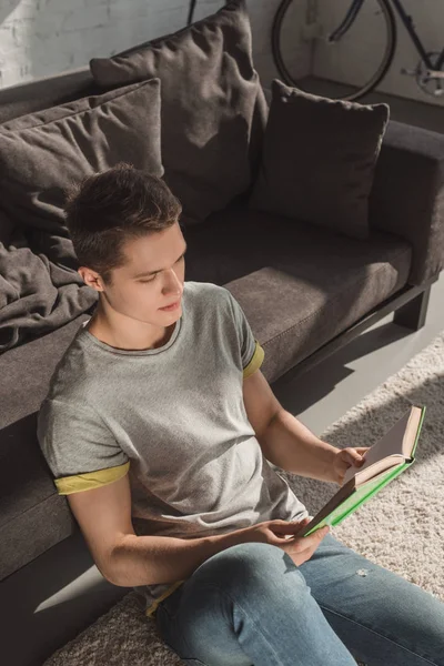 Bonito homem sentado no chão e leitura livro — Fotografia de Stock