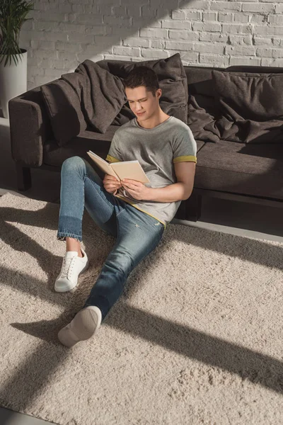 Hombre guapo leyendo libro en el suelo en casa - foto de stock