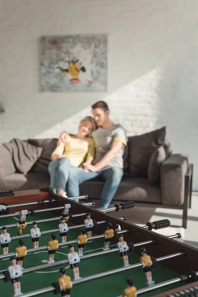 Coppia che si abbraccia e si siede sul divano in salotto a casa con biliardino in primo piano — Foto stock