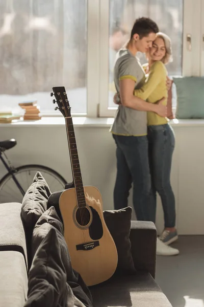 Casal abraçando em casa com guitarra acústica em primeiro plano — Fotografia de Stock