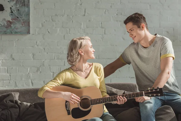 Petite amie jouant de la guitare acoustique et regardant petit ami à la maison — Photo de stock