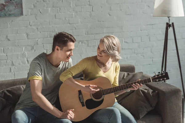 Sorrindo namorada tocando guitarra acústica para namorado em casa — Fotografia de Stock