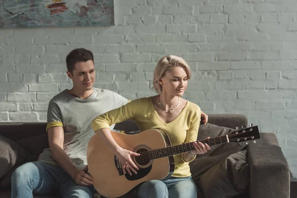 Novia tocando la guitarra acústica para el novio en casa - foto de stock