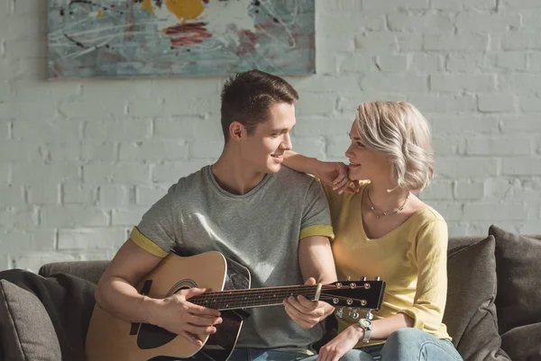 Namorado tocando guitarra acústica e olhando para a namorada em casa — Fotografia de Stock
