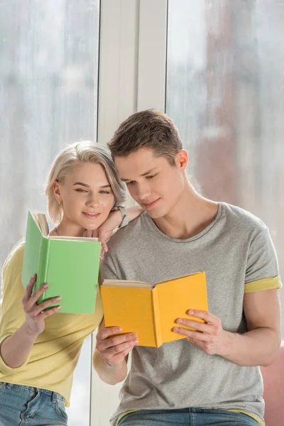 Beau couple assis sur le rebord de la fenêtre et la lecture de livres à la maison — Photo de stock