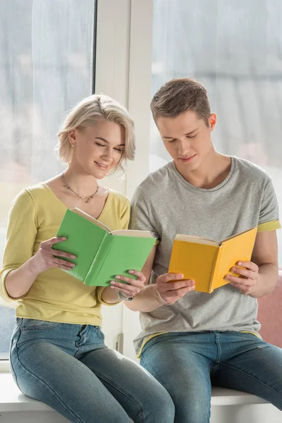 Pareja sentada en el alféizar de la ventana y leyendo libros en casa - foto de stock