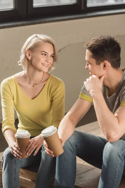 Couple souriant assis avec des tasses à café jetables à la maison — Photo de stock