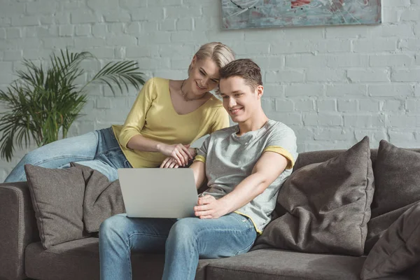 Улыбающаяся пара смотрит на ноутбук дома — стоковое фото