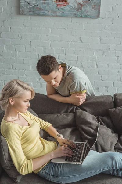 Petite amie en utilisant un ordinateur portable et petit ami regardant l'écran à la maison — Photo de stock