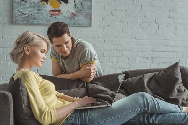 Novia usando el ordenador portátil y novio mirando la pantalla en casa - foto de stock