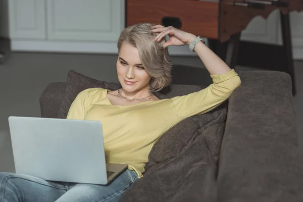 Schönes Mädchen liegt mit Laptop auf Sofa zu Hause — Stockfoto