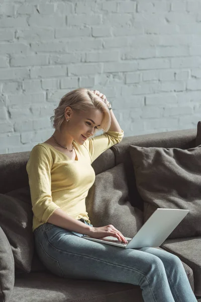 Schönes Mädchen sitzt auf dem Sofa und benutzt Laptop — Stockfoto