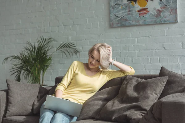 Красивая девушка сидит с ноутбуком на диване — стоковое фото