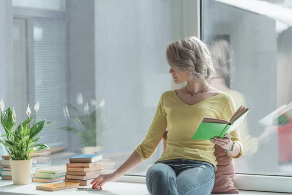 Beautiful girl holding book and taking by smartphone — Stock Photo