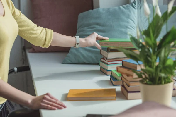 Immagine ritagliata di donna che prende libro da pila sul davanzale della finestra — Foto stock