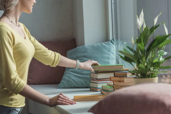 Cropped image of girl taking book from stack on windowsill — Stock Photo