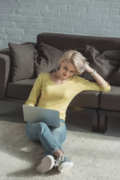 Привлекательная девушка сидит на полу и с помощью ноутбука — стоковое фото