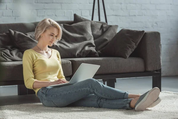 Beautiful girl leaning on sofa and using laptop — Stock Photo