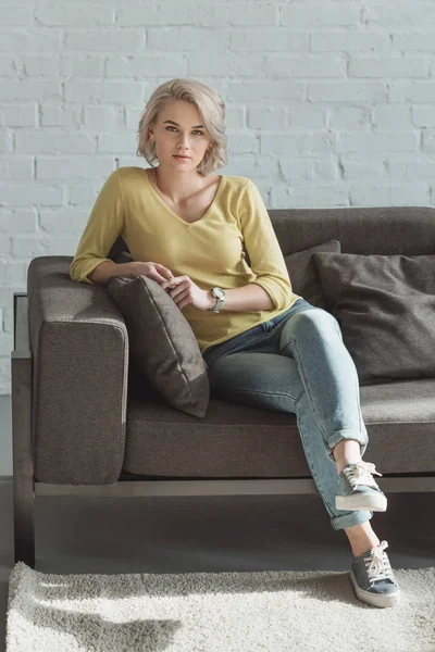 Belle fille assise sur canapé et regardant la caméra — Photo de stock