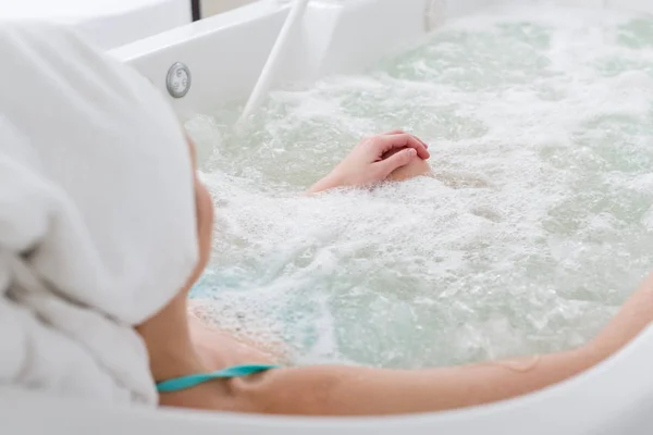 Частковий вид на жінку з рушником на голові, що розслабляється у ванні в спа-салоні — стокове фото