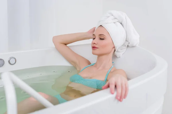 Junge Frau im Badeanzug mit Handtuch auf dem Kopf entspannt im Bad im Wellness-Salon — Stockfoto