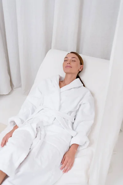Молода приваблива жінка в білому халаті з закритими очима відпочиває в спа-салоні — стокове фото