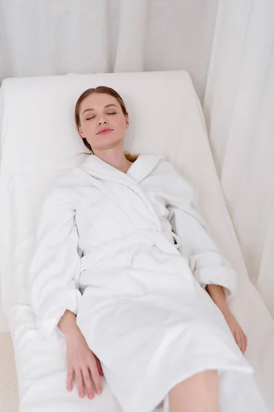 Jeune femme séduisante en peignoir blanc avec les yeux fermés reposant dans le salon de spa — Photo de stock