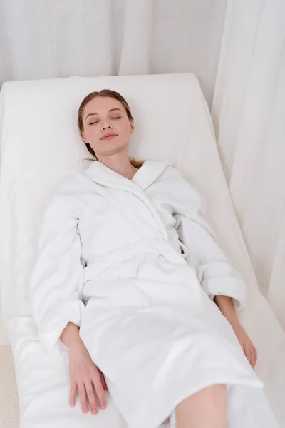 Young attractive woman in white bathrobe with eyes closed resting in spa salon — Stock Photo