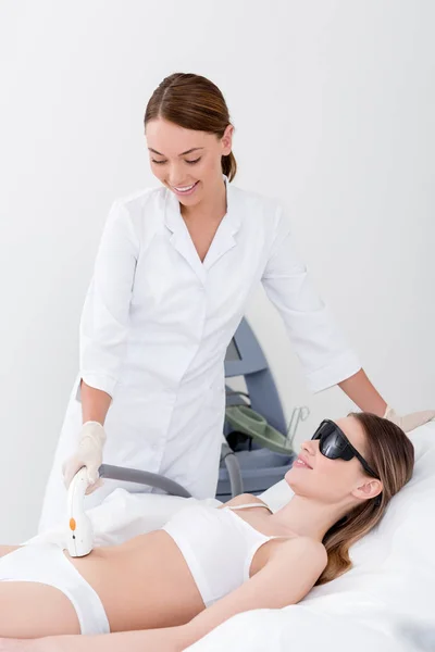 Женщина в нижнем белье, получающая лазерную процедуру удаления волос на желудке в салоне — стоковое фото