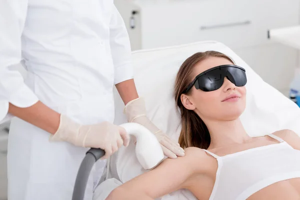 Vista parziale di donna che riceve la procedura di depilazione laser su braccio fatta da cosmetologo in salone — Stock Photo