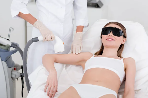 Vista parziale di donna che riceve la procedura di depilazione laser su braccio fatta da cosmetologo in salone — Foto stock
