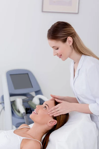 Jovem mulher recebendo massagem na cabeça feita por cosmetologist no salão — Fotografia de Stock