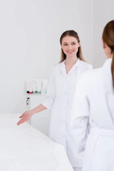 Cosmétologue souriant en manteau blanc et client dans le salon — Photo de stock