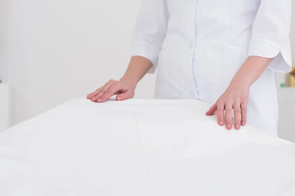 Vue partielle du cosmétologue en manteau blanc debout près de la table de massage vide dans le salon — Photo de stock