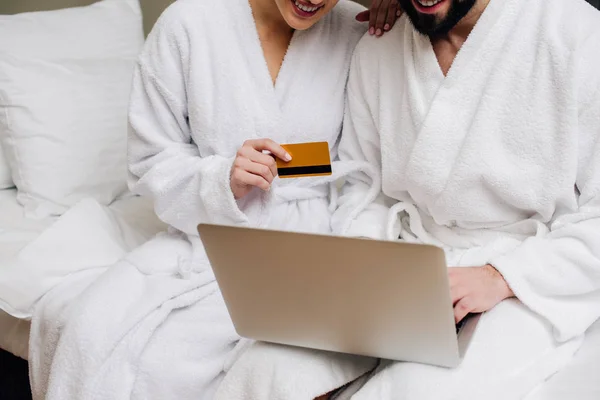 Cropped shot of couple in bathrobes making e-shopping with laptop and credit card at hotel suite — Stock Photo