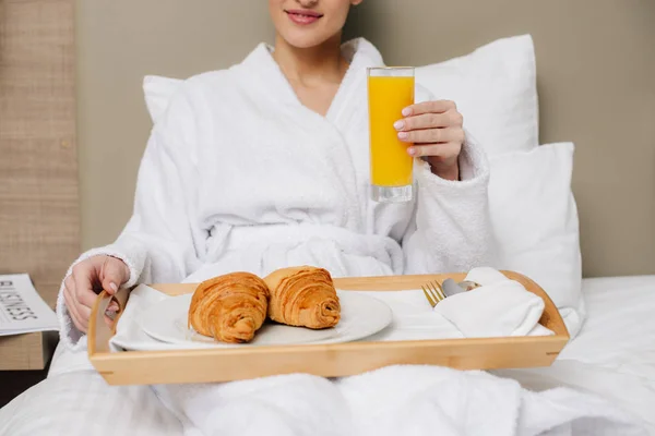 Tiro recortado de mujer en albornoz relajante en la habitación del hotel con desayuno en la cama - foto de stock