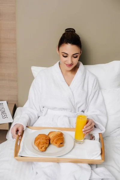 Happy woman in bathrobe relaxing at hotel room with breakfast in bed — Stock Photo