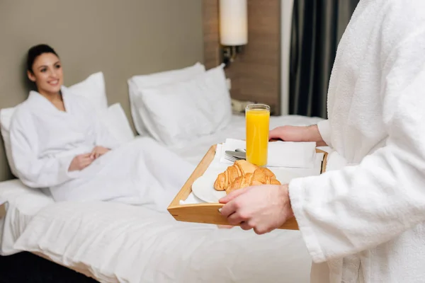 Plan recadré de l'homme portant plateau avec petit déjeuner pour petite amie alors qu'elle est assise dans le lit à la suite de l'hôtel — Photo de stock