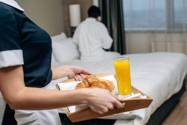 Cropped shot of maid in uniform holding tray with croissants and juice for hotel guest — Stock Photo