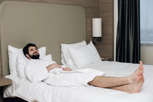 Schöner Mann im Bademantel entspannt auf dem Bett in der Hotelsuite — Stockfoto