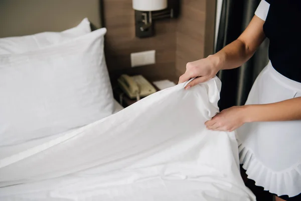 Tiro recortado de criada en uniforme haciendo cama en suite de hotel - foto de stock